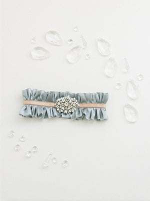 Mamie + James Charlotte silk charmeuse adjustable wedding garter with nude stretch banding and Antoinette blue silk charmeuse with rhinestone appliqué in a silver tone setting